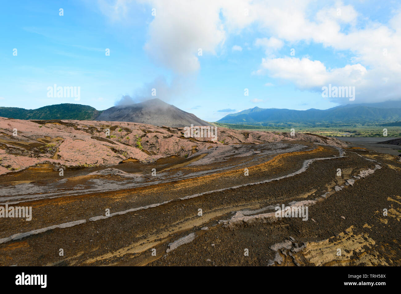 Amazing lava strata and volcanic ash patterns in the plain around Mt Yasur Volcano seen erupting in the background, Tanna Island, Vanuatu Stock Photo