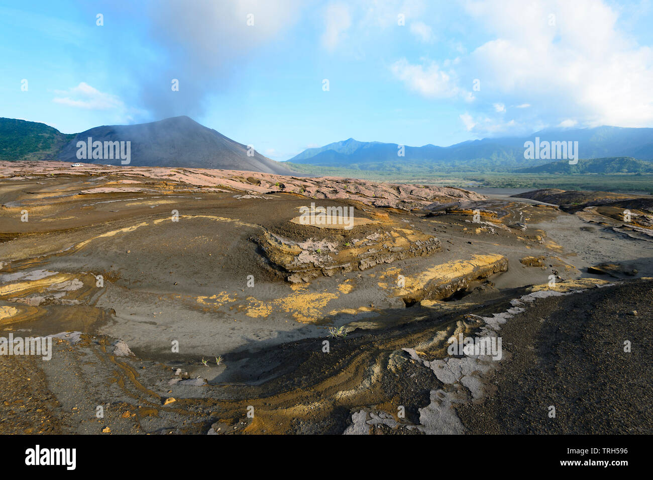 Amazing lava strata and volcanic ash patterns in the plain around Mt Yasur Volcano seen erupting in the background, Tanna Island, Vanuatu Stock Photo