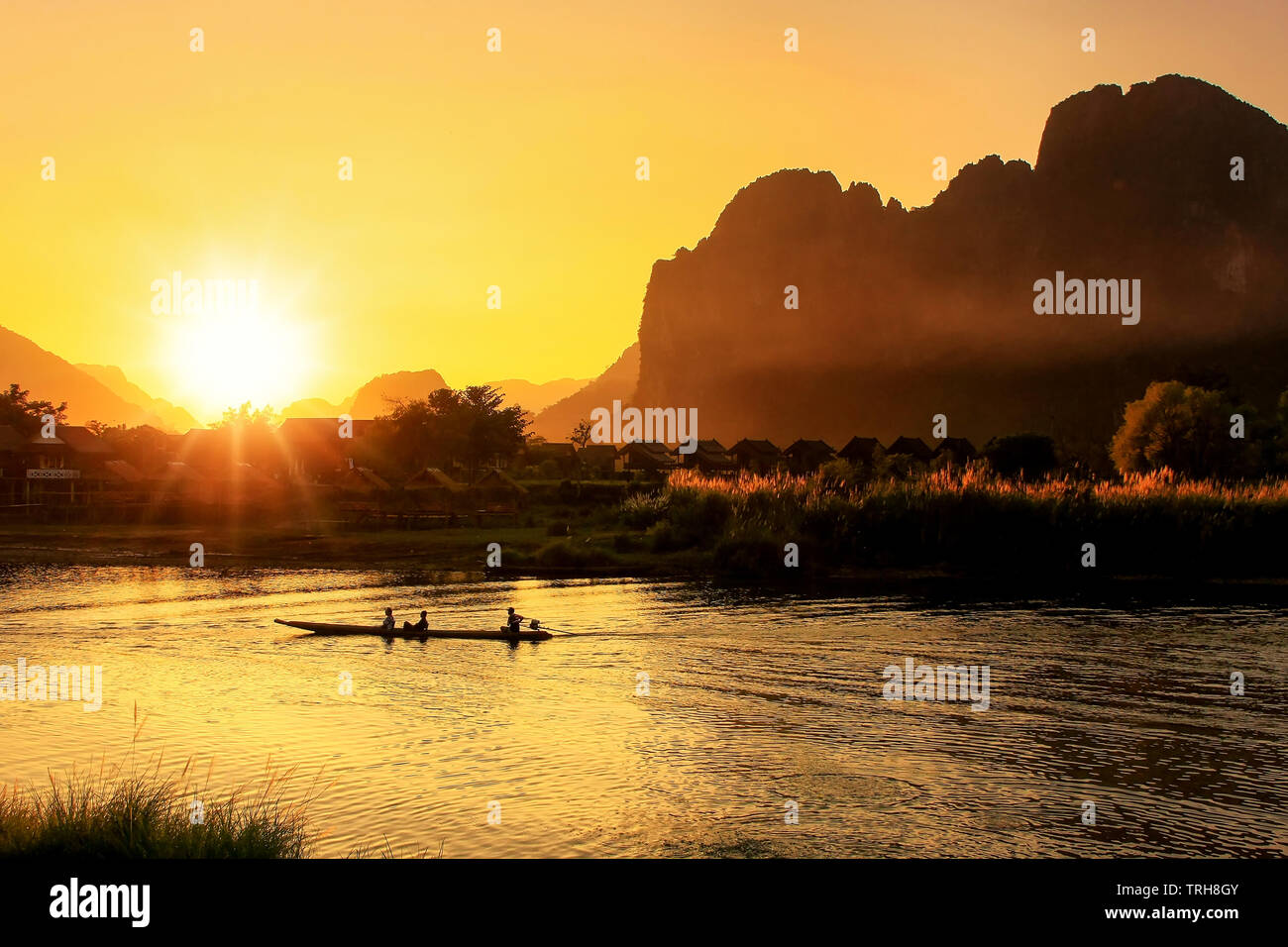Sunset over Nam Song River with silhouetted rock formations and a boat in Vang Vieng, Laos. Vang Vieng is a popular destination for adventure tourism Stock Photo