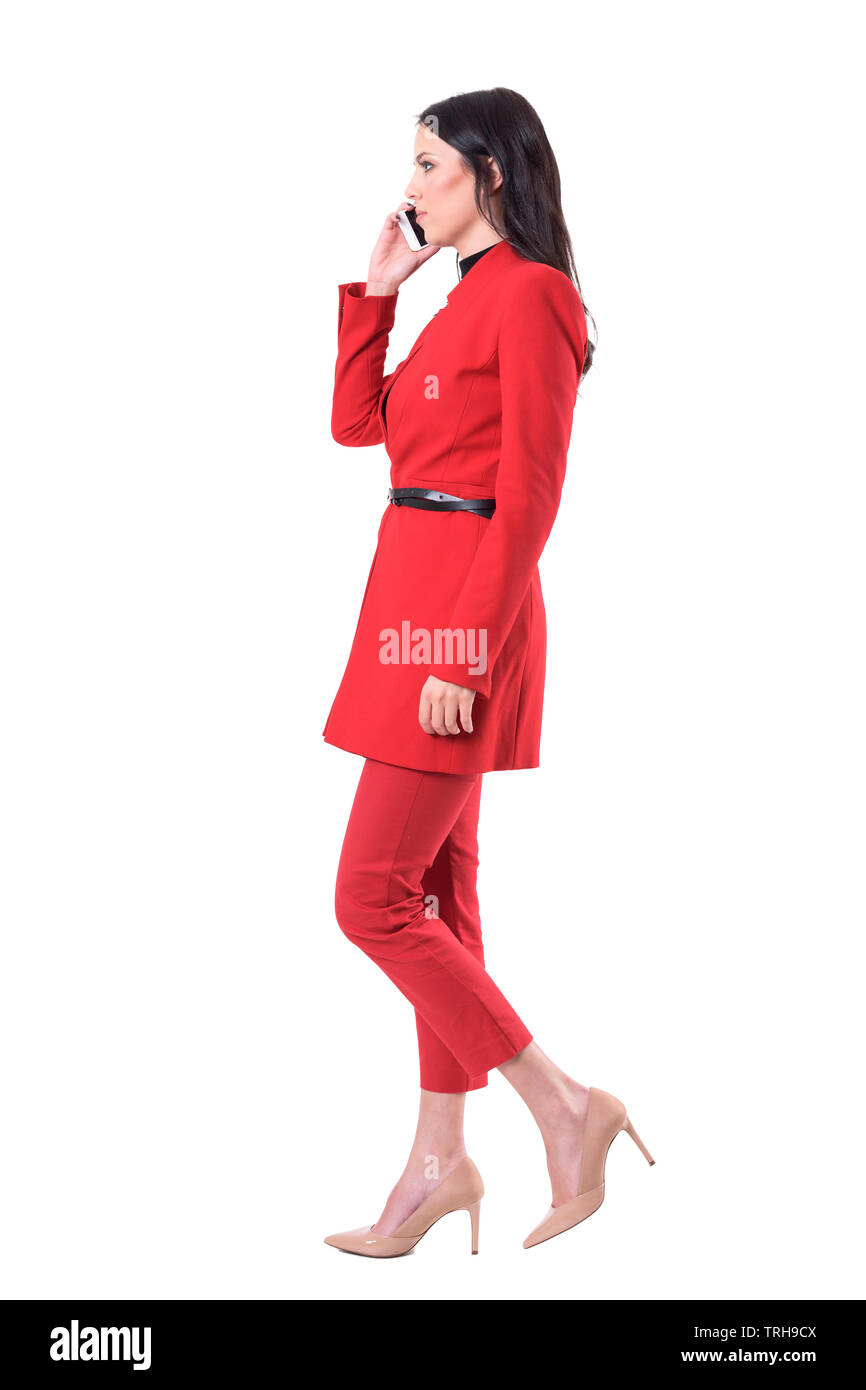 Serious busy business woman in red suit talking on the phone and walking. Full body isolated on white background. Stock Photo