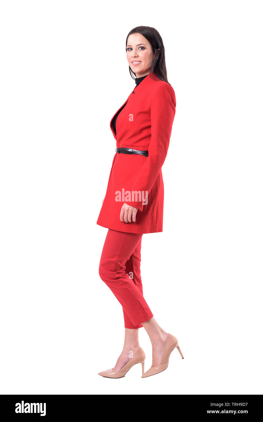 Side view of elegant business woman in red suit walking and smiling at camera. Full body isolated on white background. Stock Photo