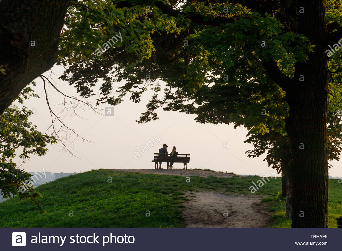 Silhouette Of A Dating Couple Sitting On A Park Bench Watching The