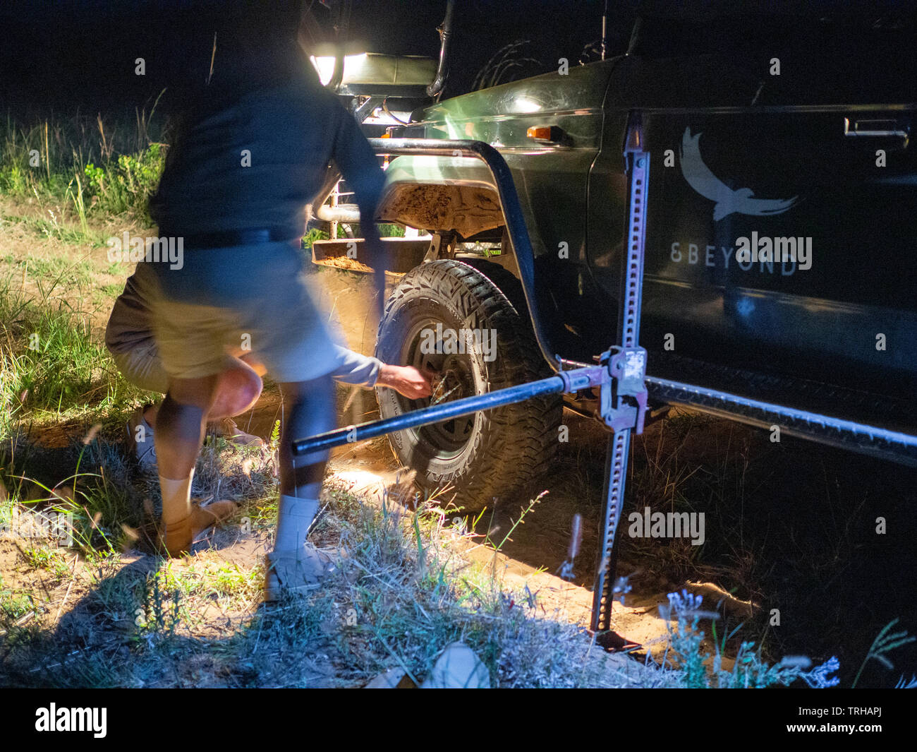 A guide and tracker change the tire of their car while on night safari at the Phinda Private Game Reserve in South Africa. Stock Photo