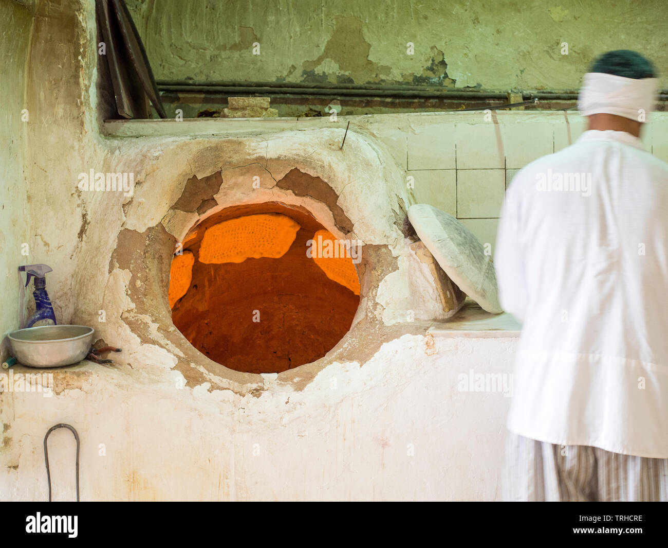A man baking naan bread in a traditional wood fired oven, known as a