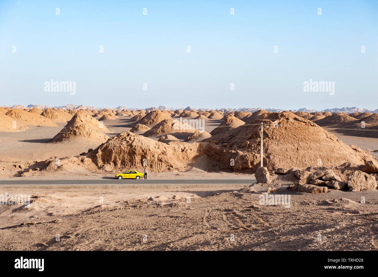 A car parked by the side of the road with yardangs in the background in the Lut Desert in Shahad, Iran. Known as kaluts in Iran, yardangs are geologic Stock Photo