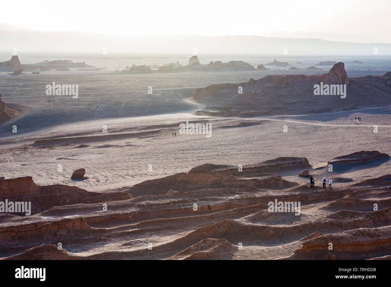 Tourists watch the sun go down over yardangs in the Lut Desert in Shahad, Iran. Known as kaluts in Iran, yardangs are geological formations that have Stock Photo