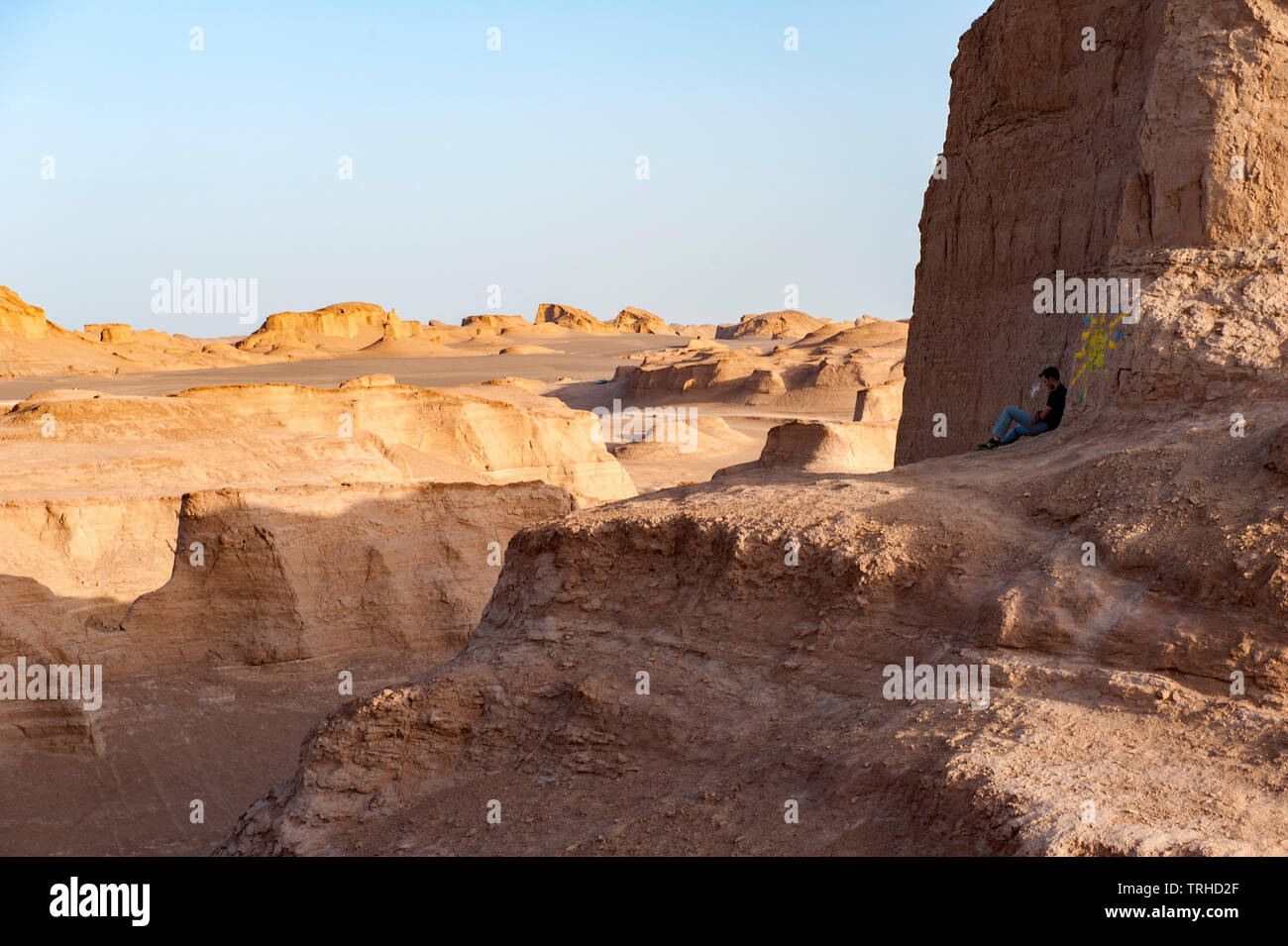 A tourist watches the sun go down over yardangs in the Lut Desert in Shahad, Iran. Stock Photo