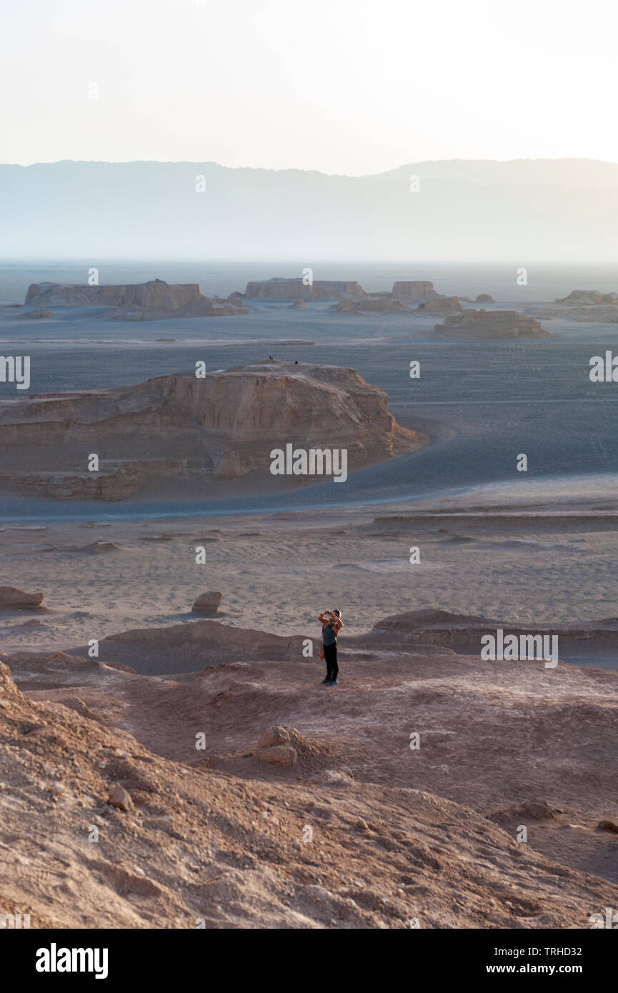 Tourists watch the sun go down over yardangs in the Lut Desert in Shahad, Iran. Known as kaluts in Iran, yardangs are geological formations that have Stock Photo