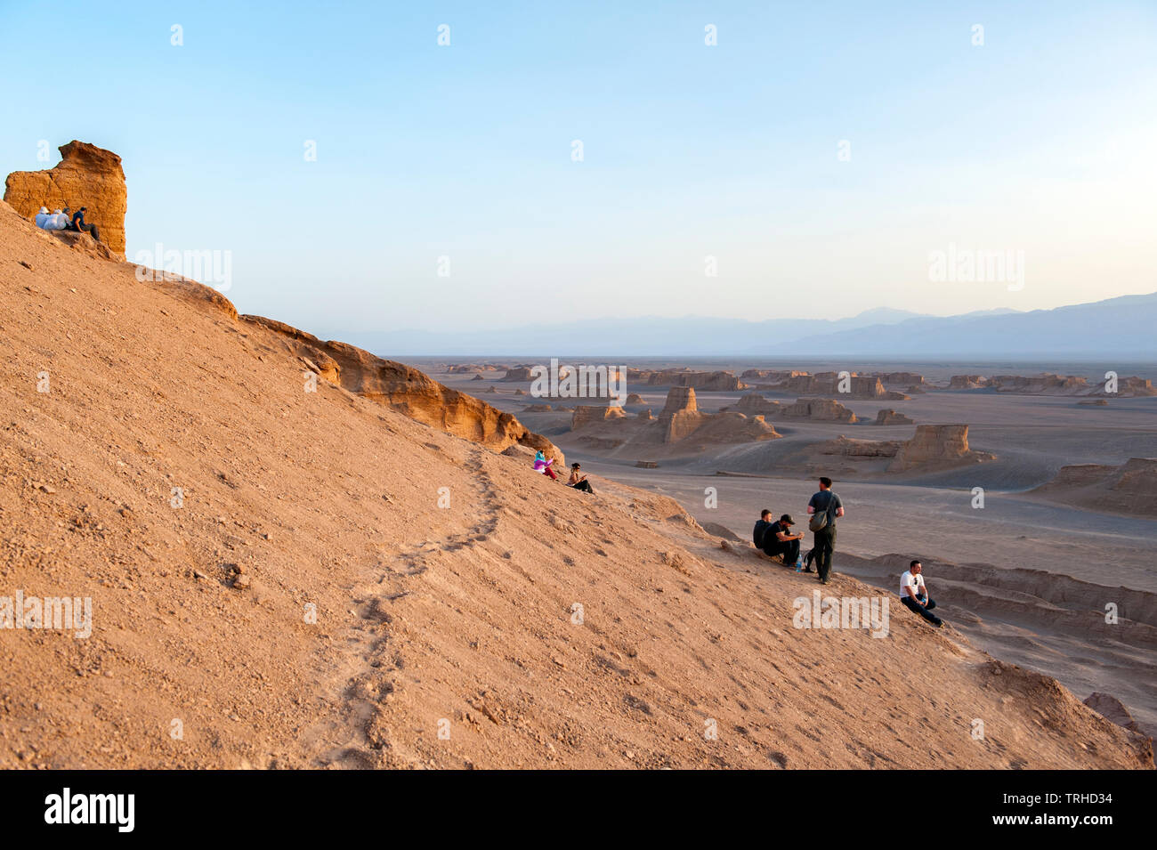 Tourists watch the sun go down over yardangs in the Lut Desert in Shahad, Iran. Known as kaluts in Iran, yardangs are geological formations. Stock Photo
