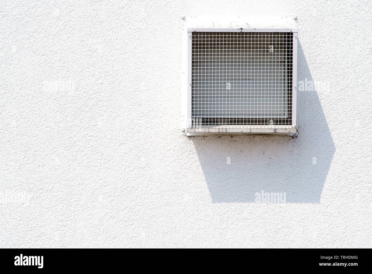 A square ventilation grille casts a shadow on a bright plaster facade. Stock Photo