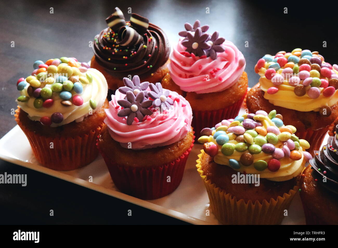 close up of a plate of cupcakes decorated with mini smarties and chocolate and sprinkles and sugar flowers Stock Photo Alamy