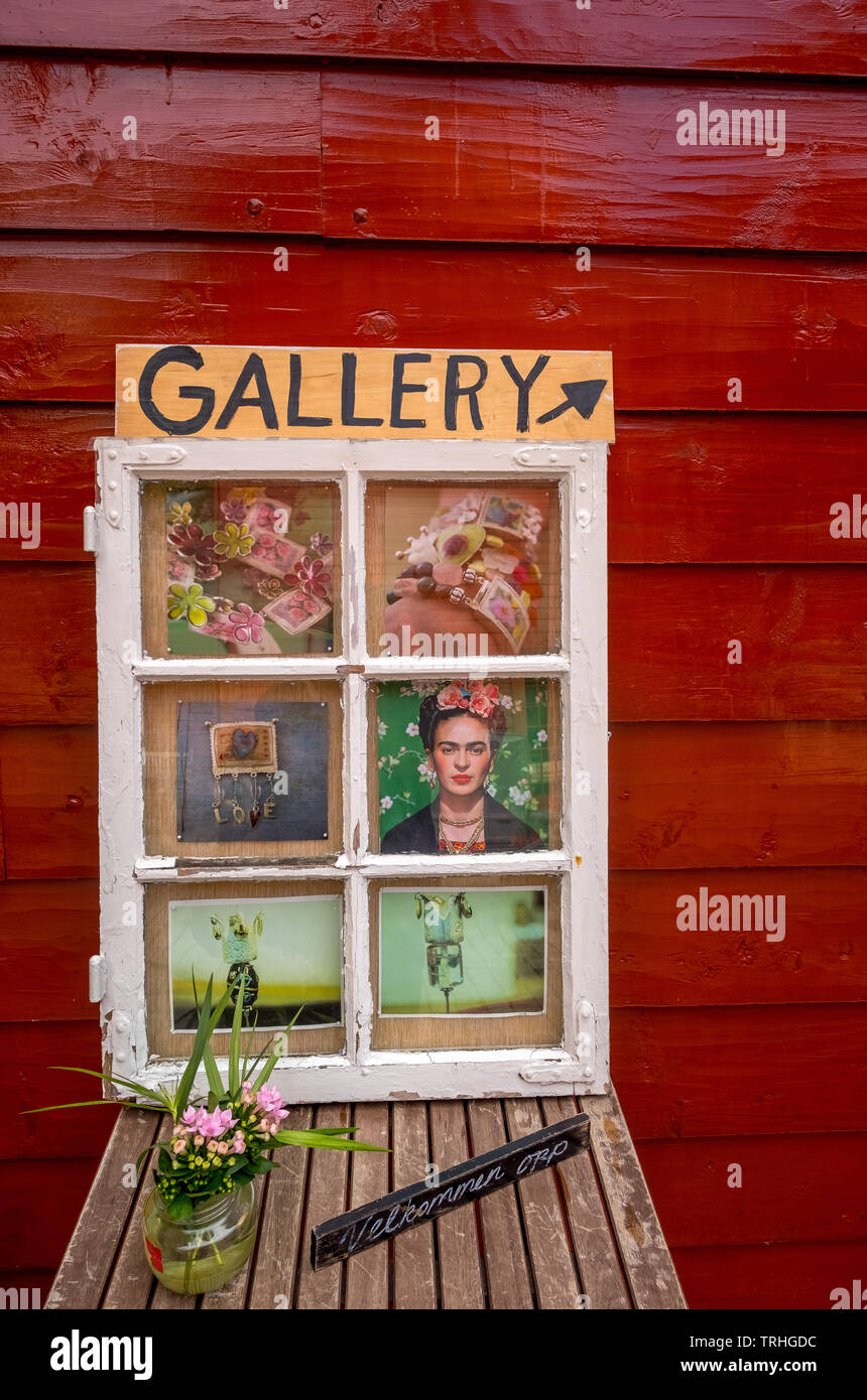 white wooden window on a wooden table with flowers and welcome sign, with playful images in front of a red wooden house wall with signs to the Gallery Stock Photo