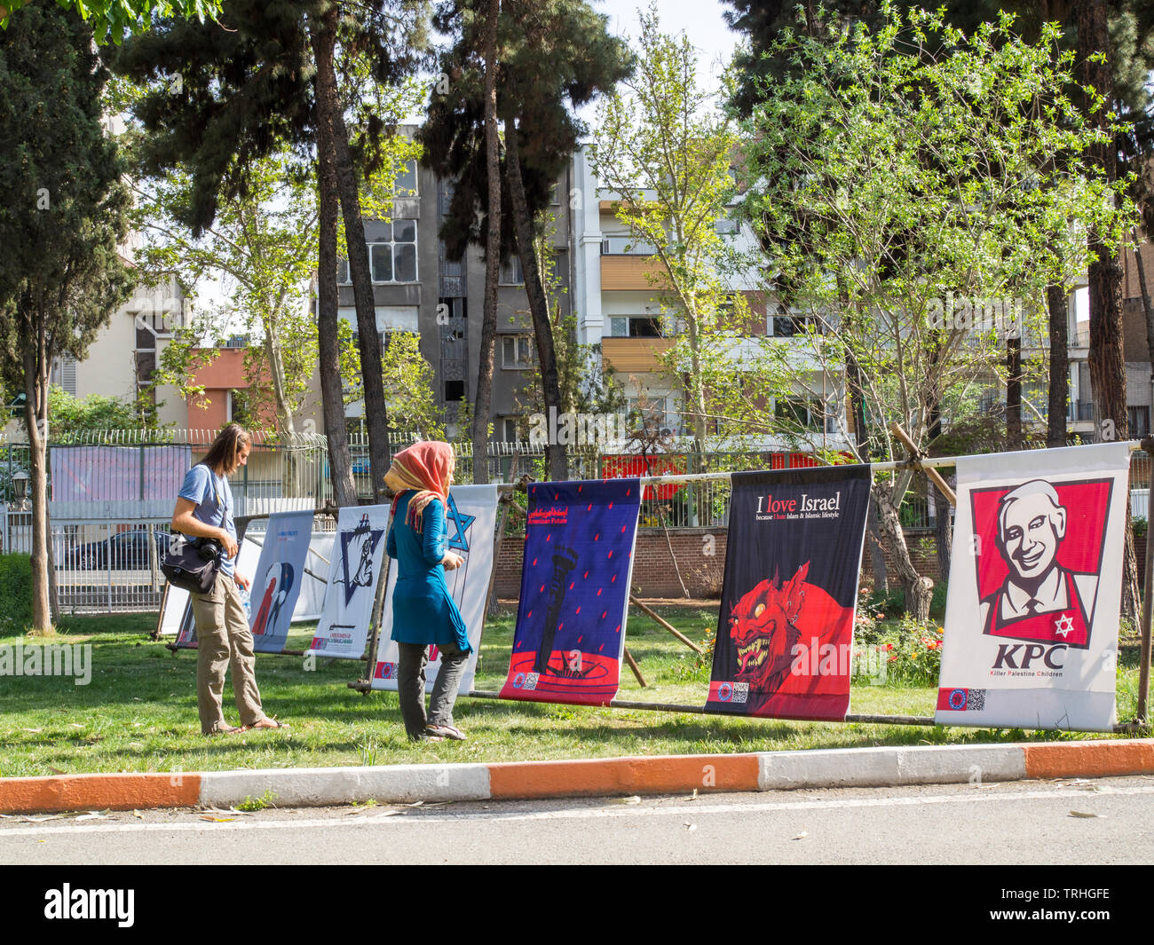Tourists walk among propaganda posters in the Museum- Garden of Anti Arrogance housed in the former American embassy in Tehran. The embassy was seized Stock Photo