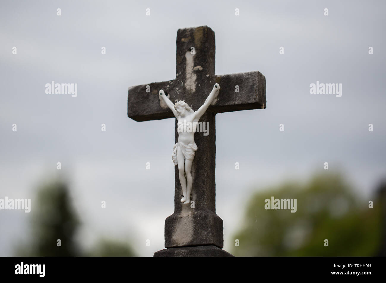 Close up of Jesus on the cross. The Jesus figure is entirely made of white stone. The cross and figure are part of a gravestone / headstone. Stock Photo