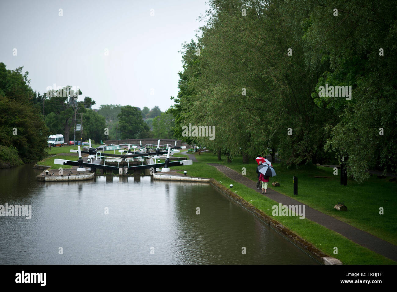 People shelter from the rain during a downpour as they walk along the tow path past Hatton Locks on the Grand Union Canal. June 4 2019. Stock Photo