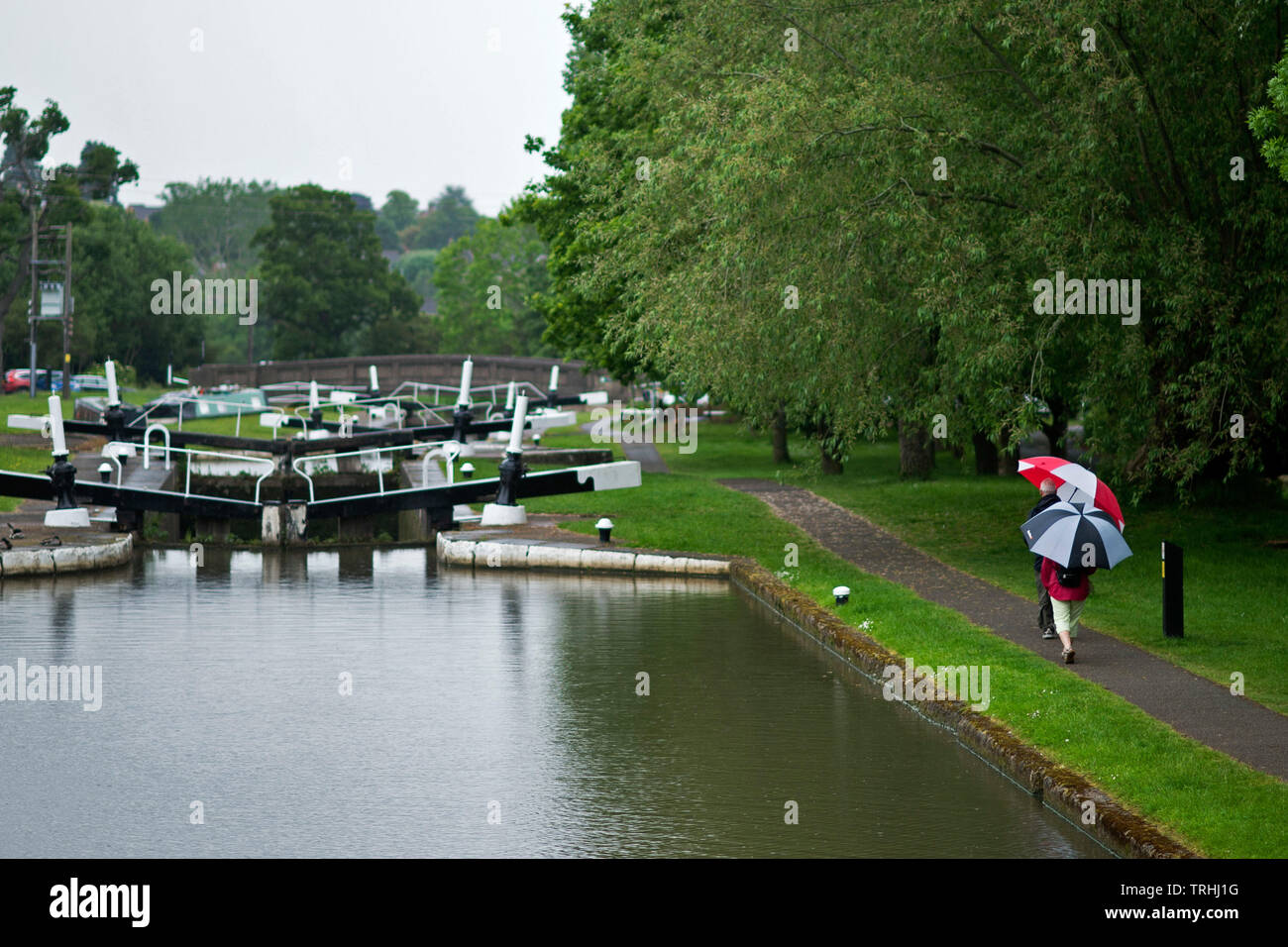 People shelter from the rain during a downpour as they walk along the tow path past Hatton Locks on the Grand Union Canal. June 4 2019. Stock Photo