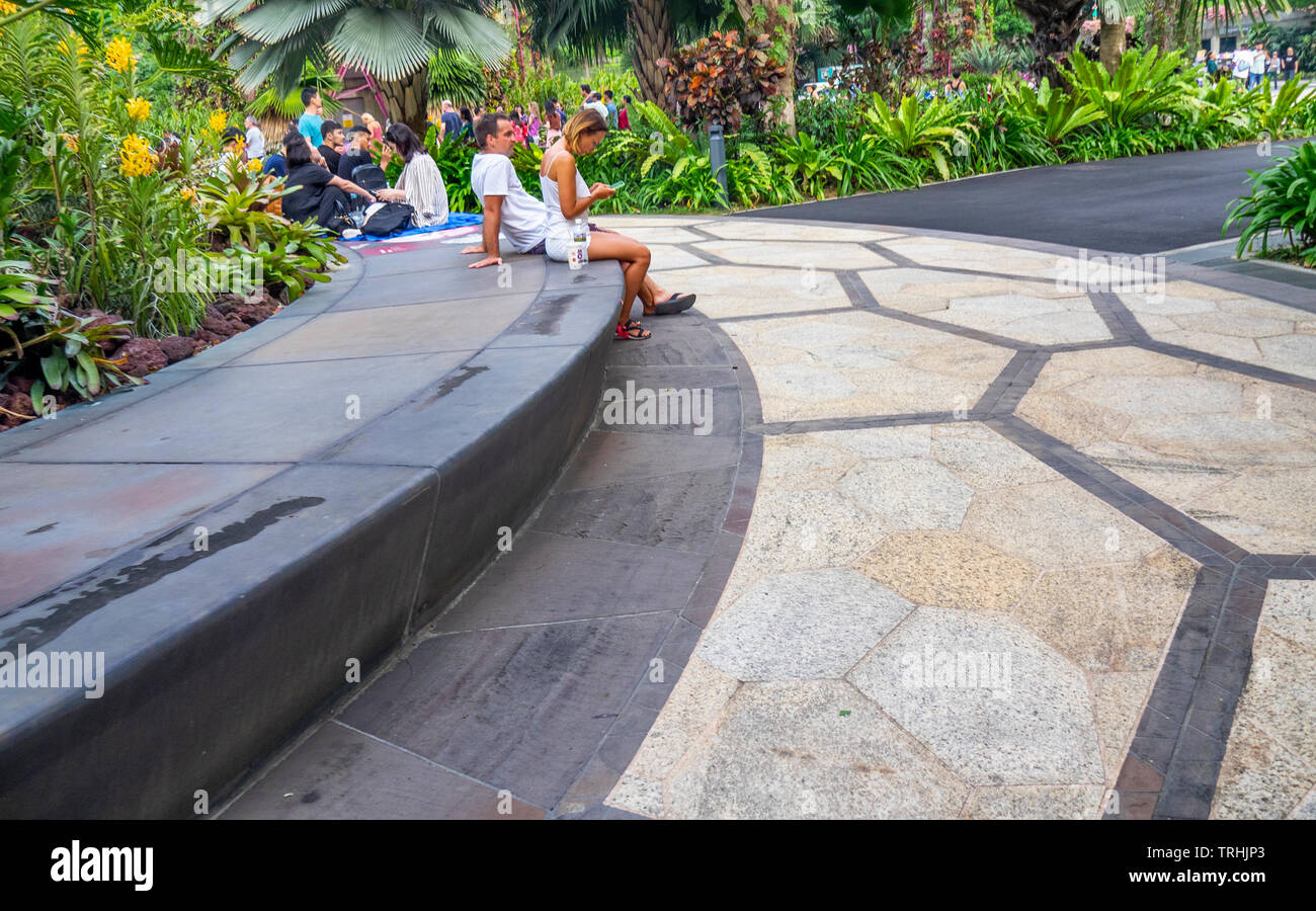 Tourists sitting at the concrete base of a Supertree at Gardens by the Bay Singapore. Stock Photo