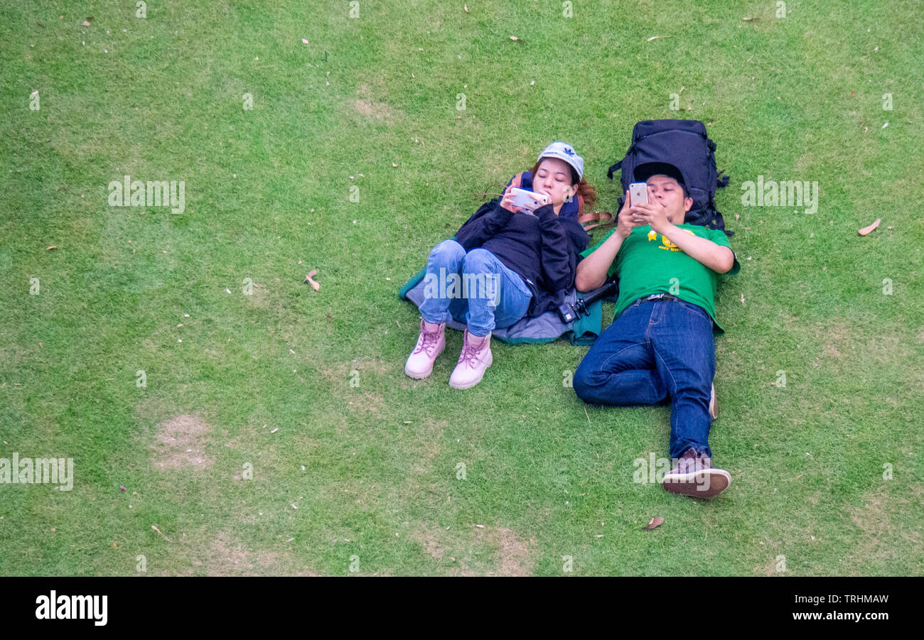 Couple lying on the lawn and both browsing on their mobile telephones at Gardens by the Bay Singapore. Stock Photo