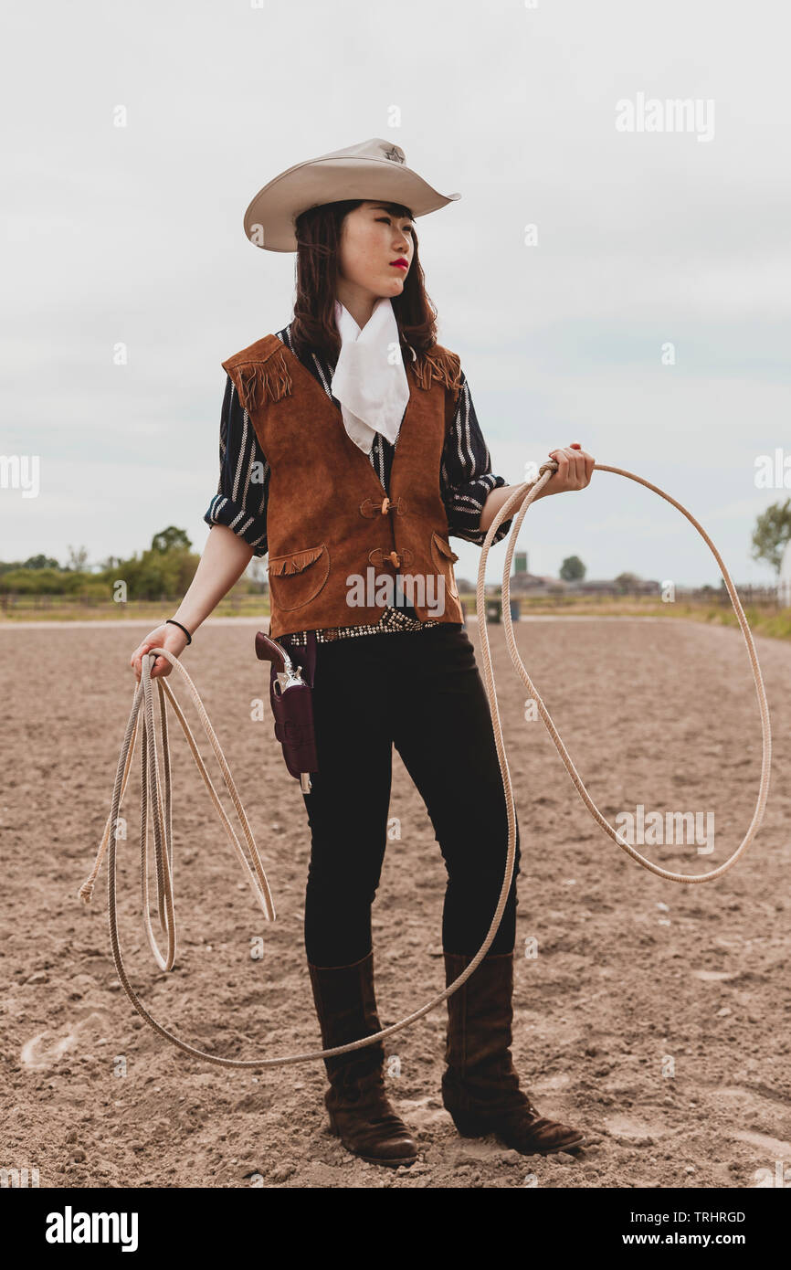 pretty Chinese cowgirl throwing the lasso in a horse paddock on a