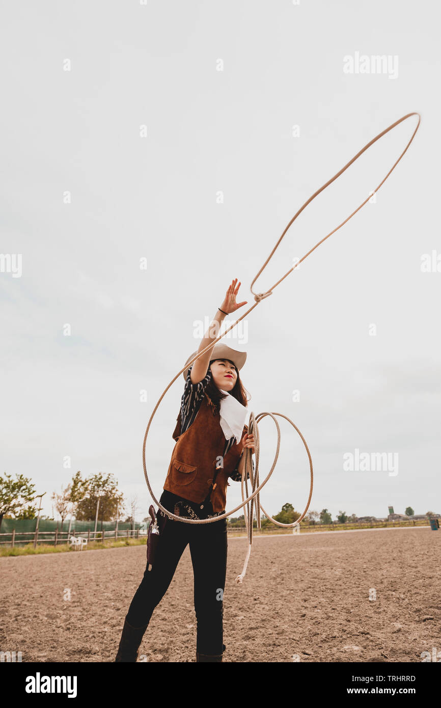 pretty Chinese cowgirl throwing the lasso in a horse paddock on a wild west farm Stock Photo