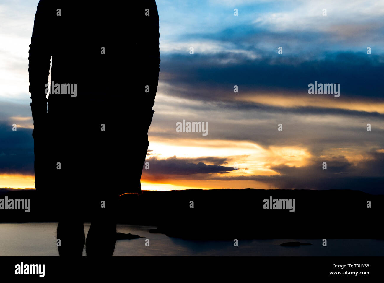 Silhouette of man overlooking mountains and water at sunset Stock Photo