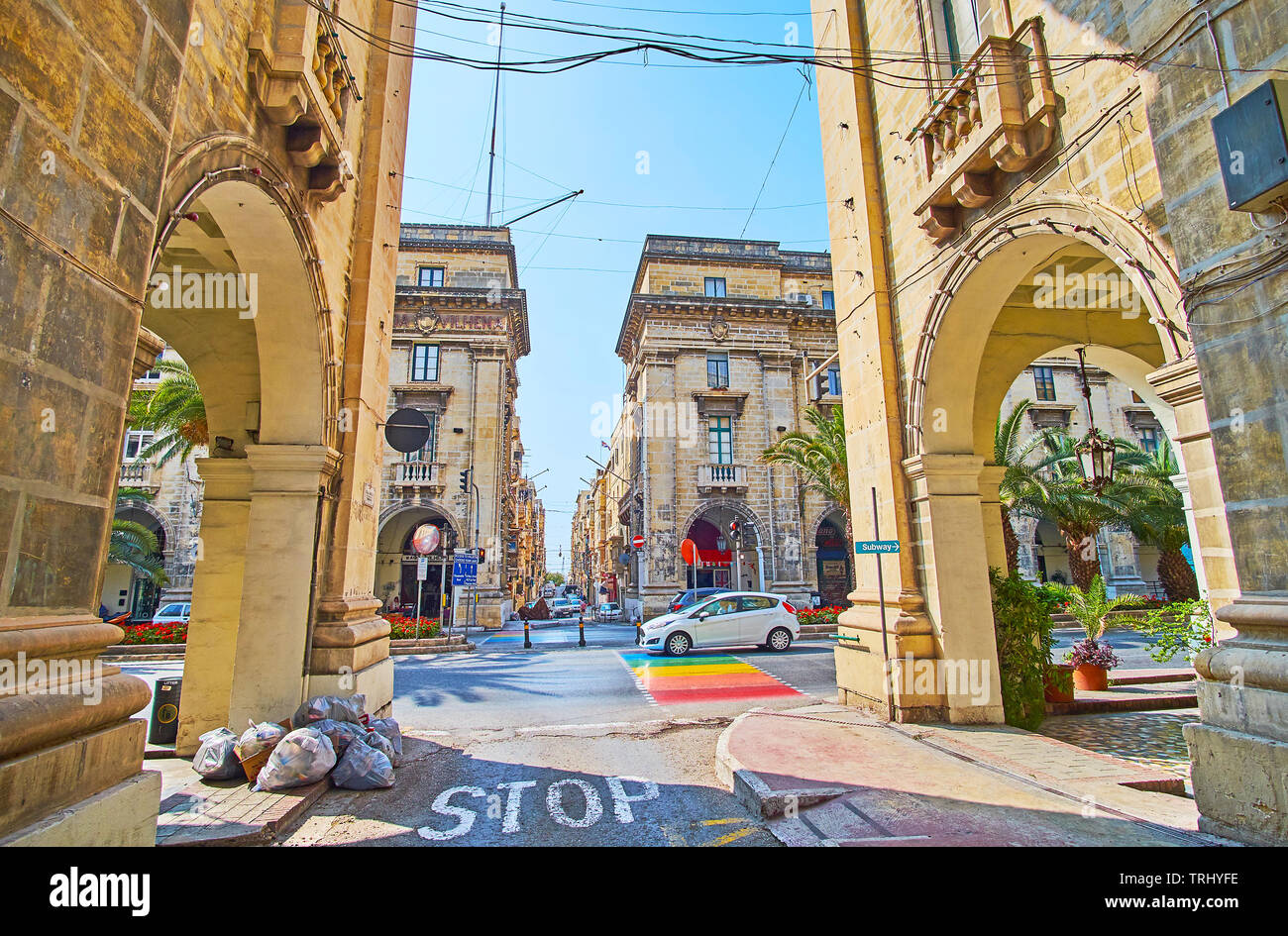 FLORIANA, MALTA - JUNE 19, 2018: The view on wide St Anne avenue through the narrow stone street, lined with historical edifices and trade arcades, on Stock Photo