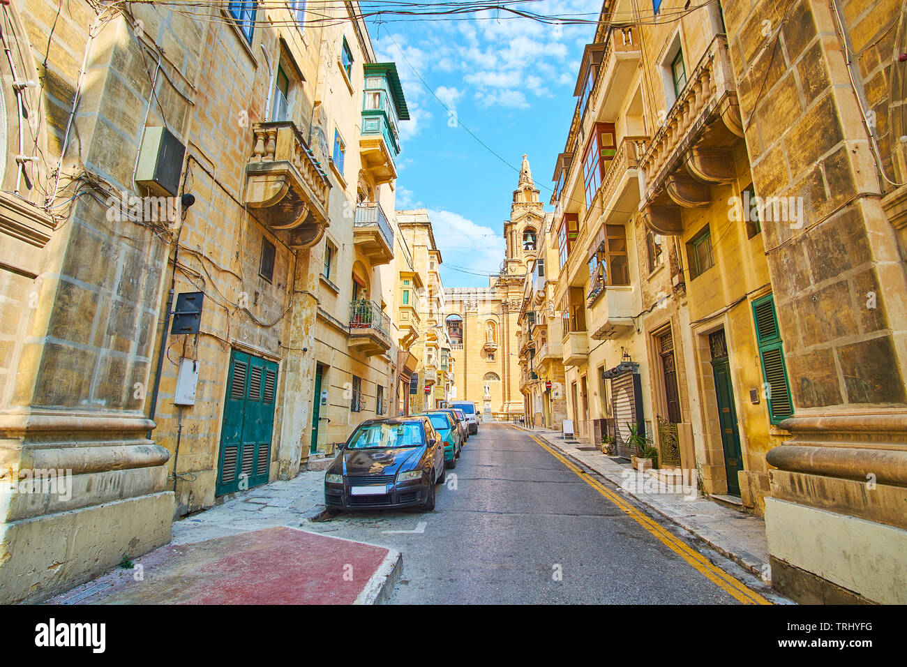 The narrow street, lined with old residential edifises wnds with side wall of St Publius Parish church, Floriana, Malta. Stock Photo