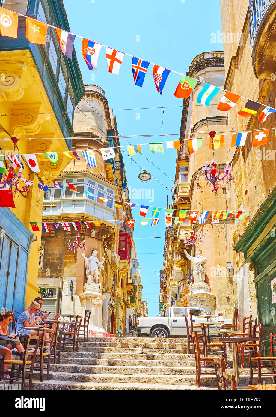 VALLETTA, MALTA - JUNE 19, 2018: The colorful flag garlands flutter in the wind above the narrow street of St Lucia, on June 19 in Valletta Stock Photo