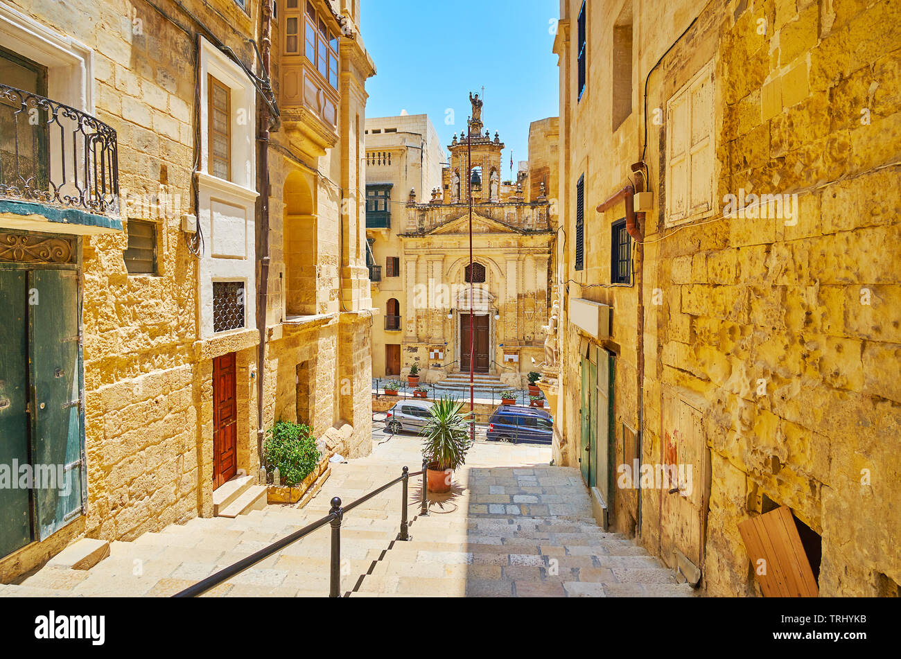 The view on carved facade of medieval St Lucy church from the narrow descent of St Lucia street, Valletta, Malta. Stock Photo