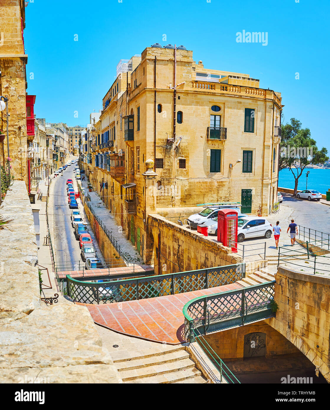 The long and narrow Lvant street runs under the small pedestrian bridge, it's lined with historical residential buildings, Valletta, Malta. Stock Photo