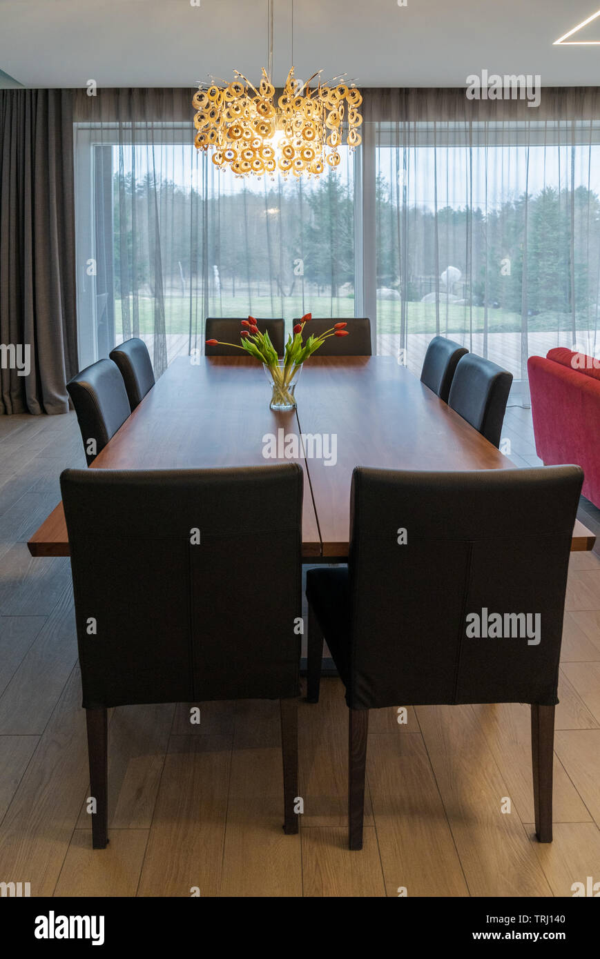 Brown wooden large dining table with chairs in a spacious, bright living room in a private house. The vase with flowers stands on a table Stock Photo
