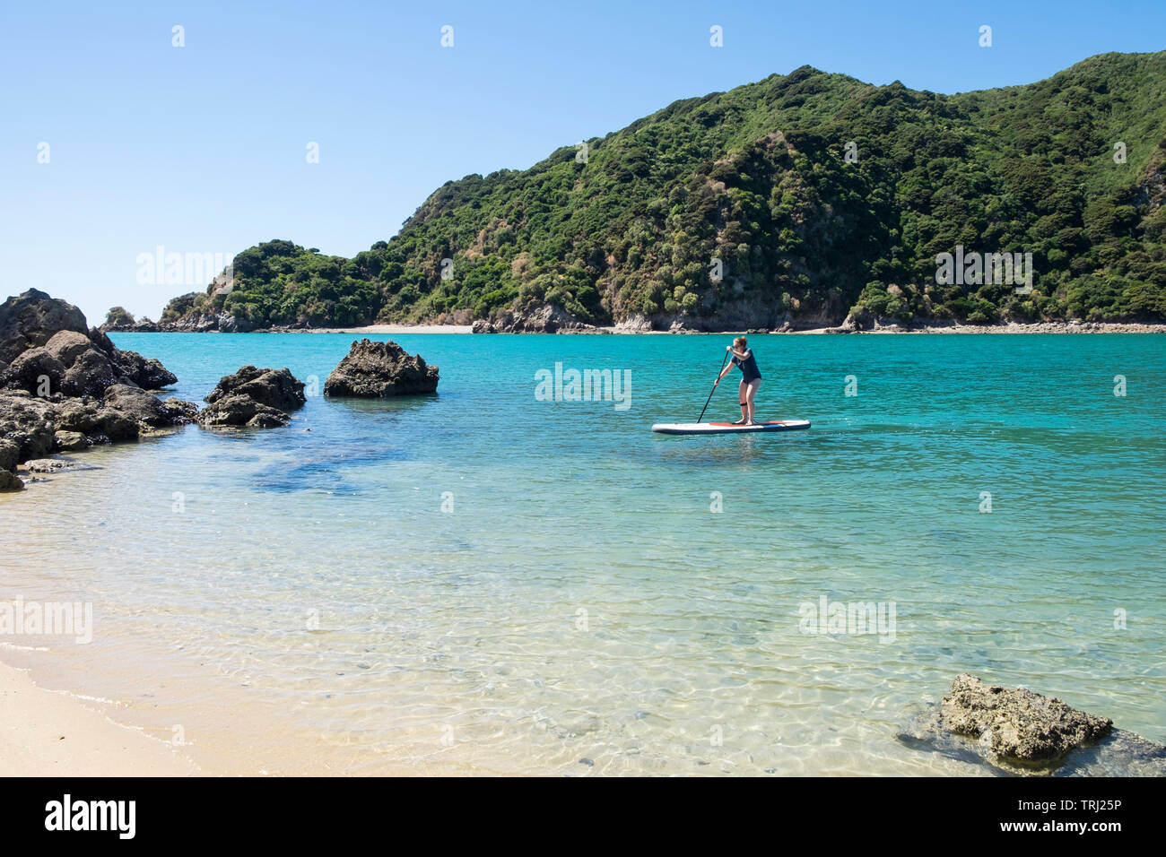 A woman paddle boarding in beautiful blue water at Tata Beach, Golden