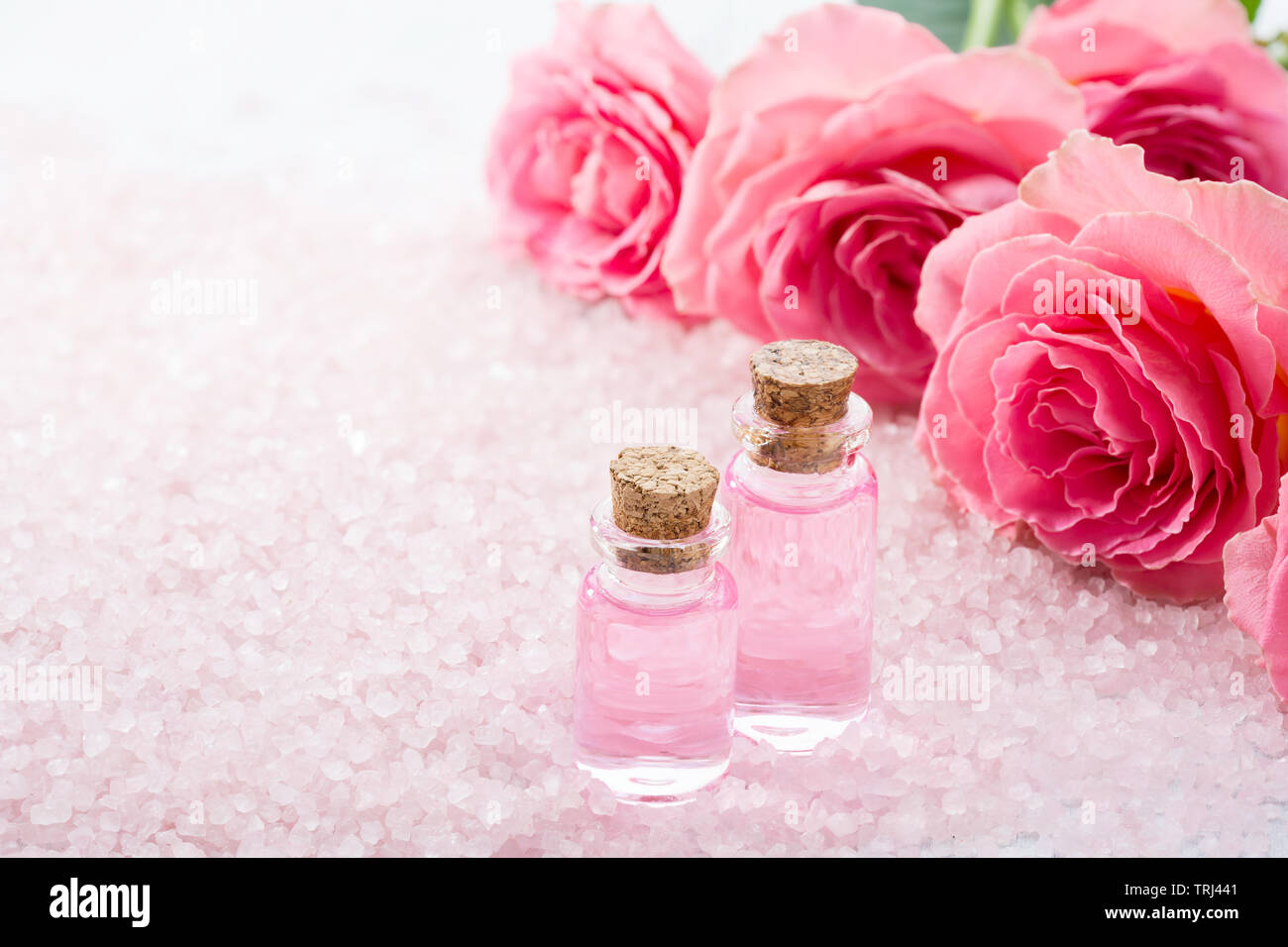 Two bottles with rose oil, spa salt crystals and pink roses. Stock Photo