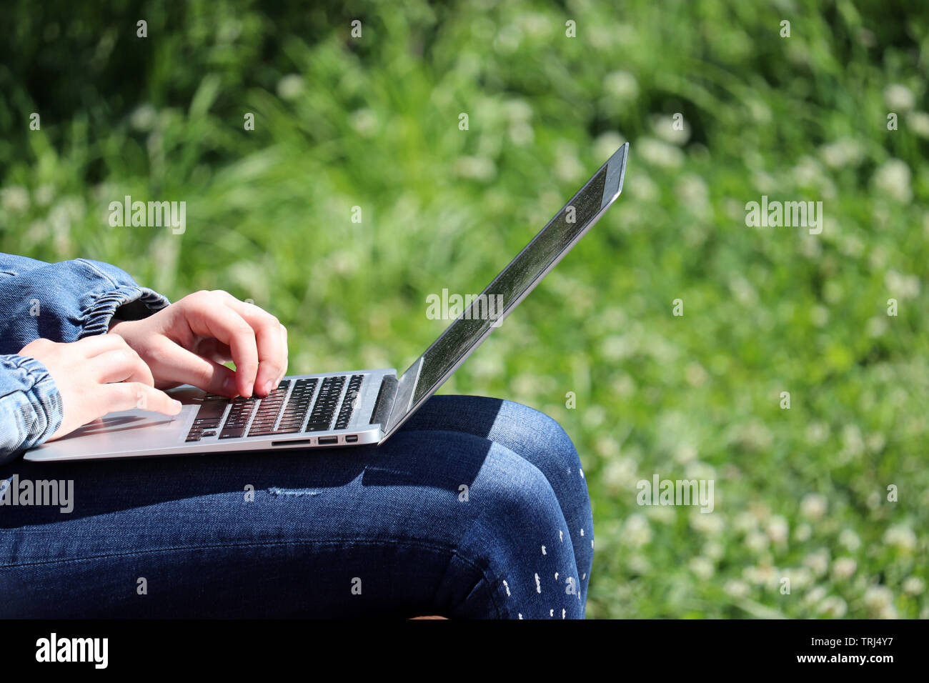 Woman sitting with a laptop on a bench in a summer park. Female hands on a keyboard, concept of student, working outdoor, businesswoman, online Stock Photo