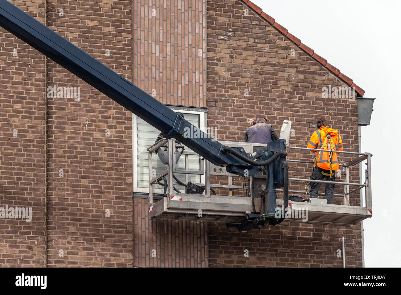 construction workers are standing on a platform of a machinery crane near a wall of an apartment Stock Photo