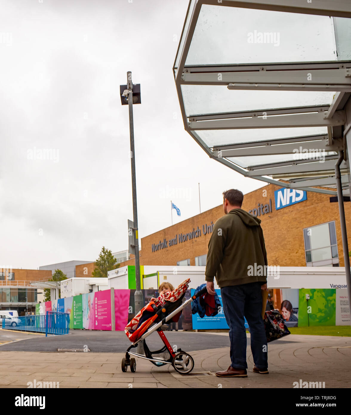 Norwich, Norfolk, UK. 18 May 2019. Candid photos - Man waiting outside at the NHS Norwich University Hospital with his baby daughter in a pushchair waiting for a taxi Stock Photo