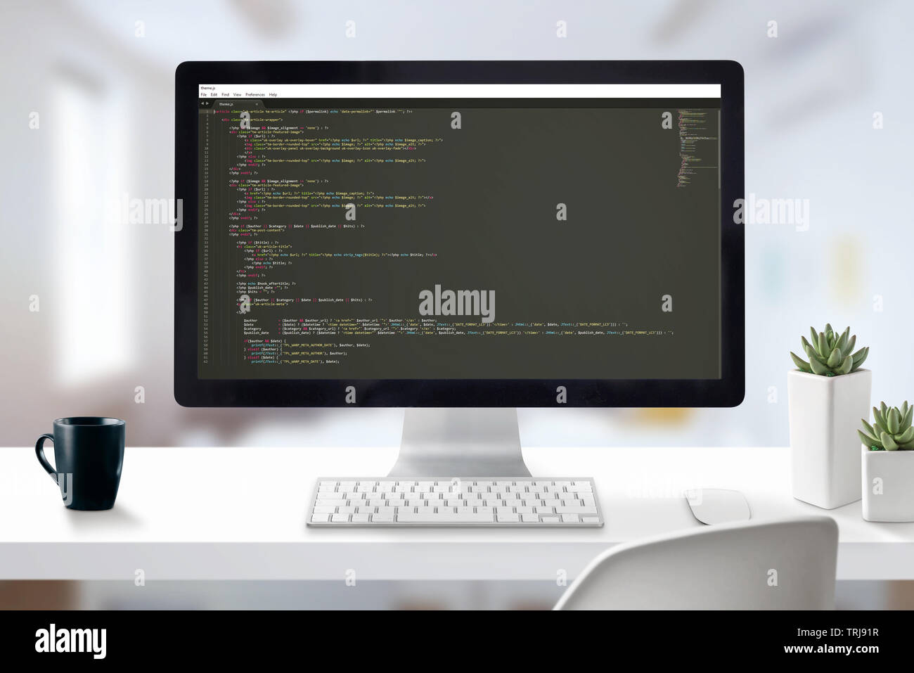 Web developer computer with javascript code on display. Work desk close-up scene with office in background. Stock Photo