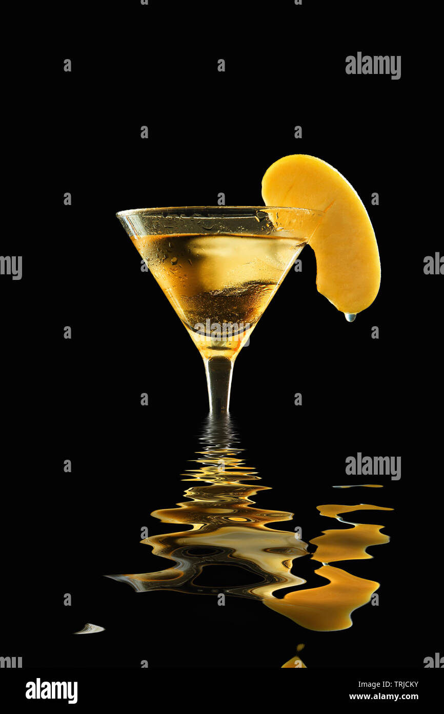 Fresh appletini in a sweaty cocktail glass with melting ice, garnished with apple slice with hanging waterdrop, flooded and reflected on water, agains Stock Photo