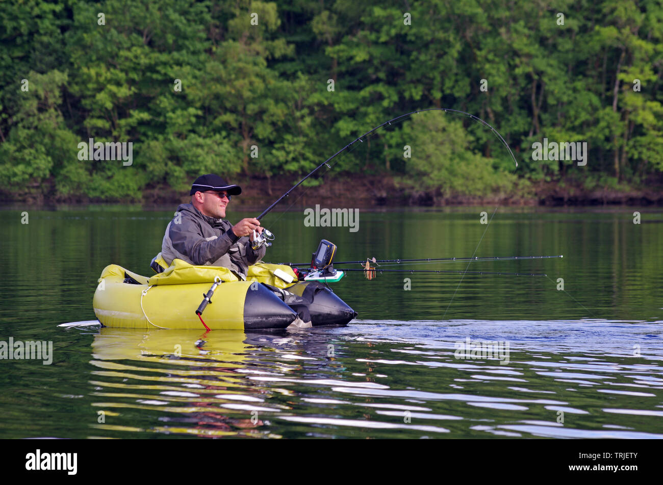 A fisherman fight against a pike. The man is sitting in the fishing inflatable boat and he use flippers to move on the water. He also use a sonar Stock Photo