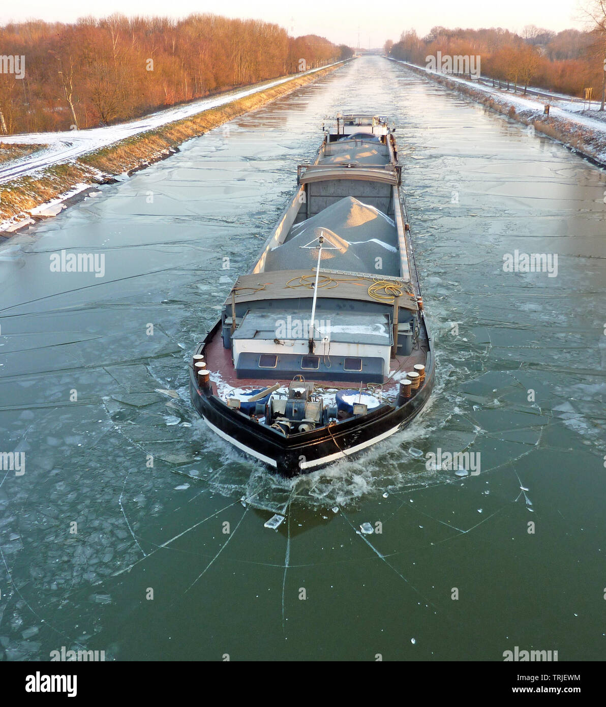 A barge transporting material sailing on a small frozen canal Stock Photo
