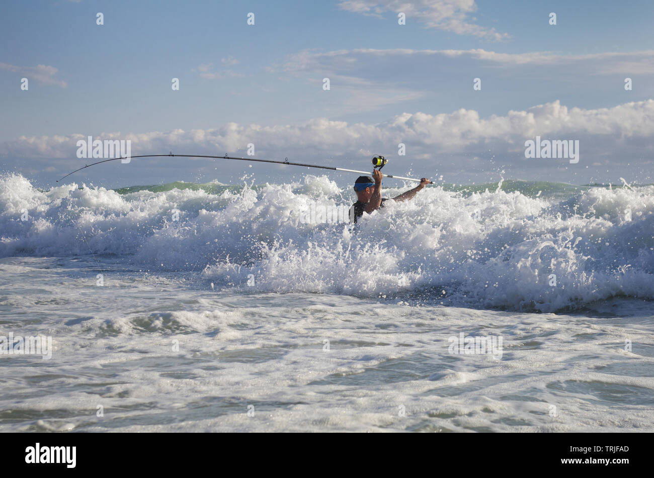 Surf fisherman into the waves try to cast the line. Sea fishing, saltwater fishing Stock Photo