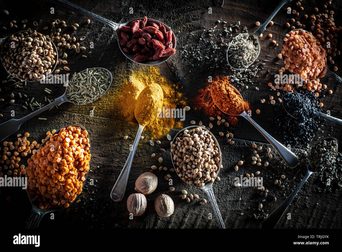Selection of spices on old antique silver spoons, turmeric, lentils, mustard seeds, nutmeg, cumin poppy agains a dark wood background shot from above Stock Photo
