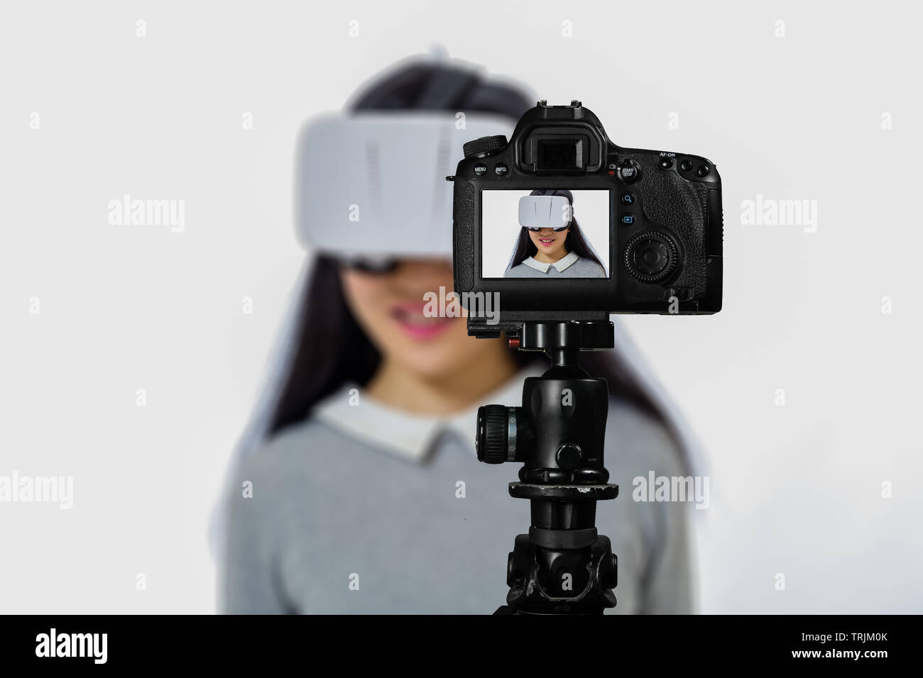 Focus on live view on camera on tripod, teenage girl using VR goggles image on back screen with