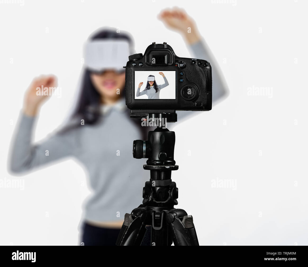 Focus on live view on camera on tripod, teenage girl using VR goggles image on back screen with