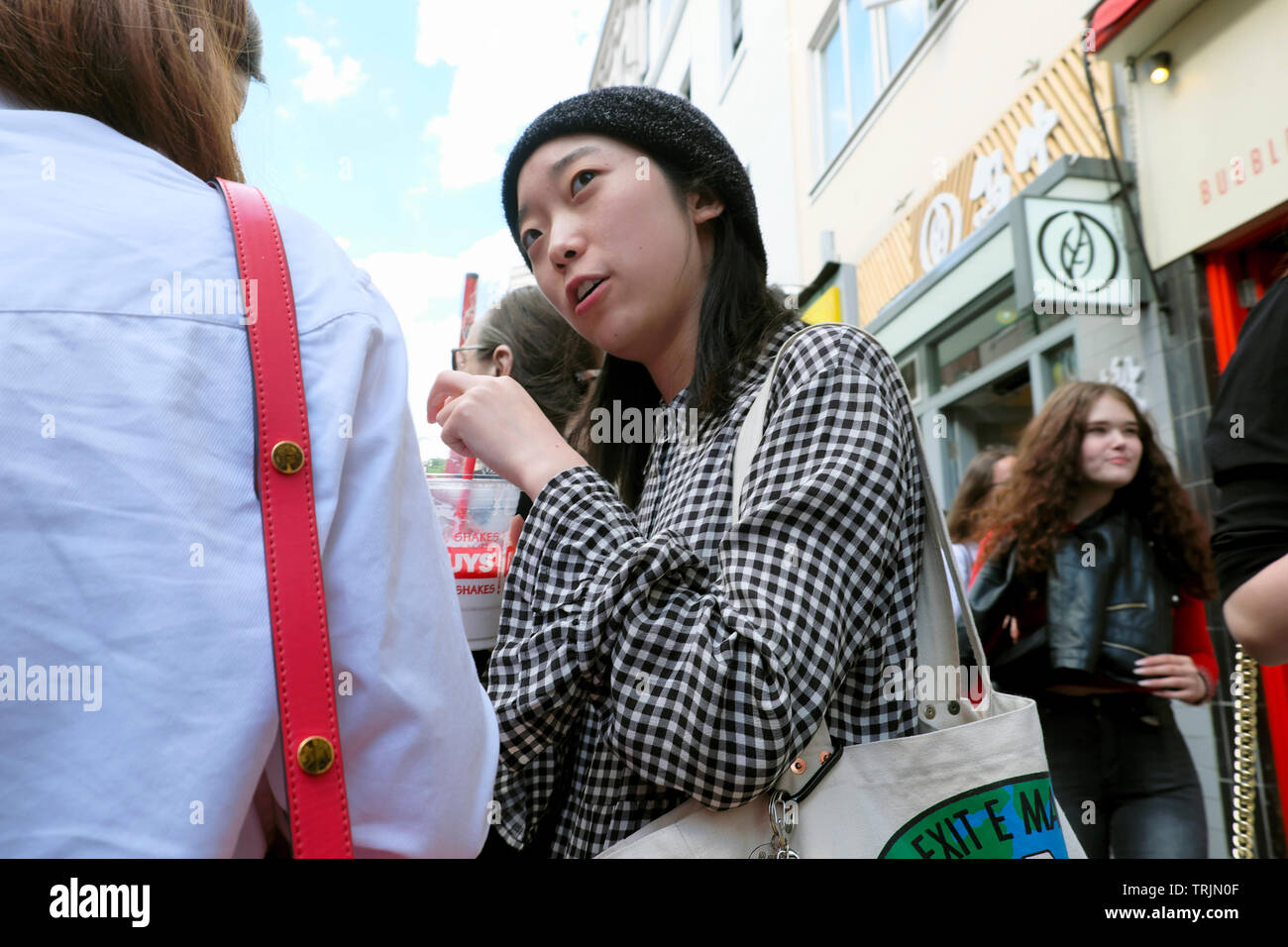 Young Chinese woman wearing black and white check shirt on Wardour Street with plastic cup & straw in Chinatown London W1 England UK   KATHY DEWITT Stock Photo