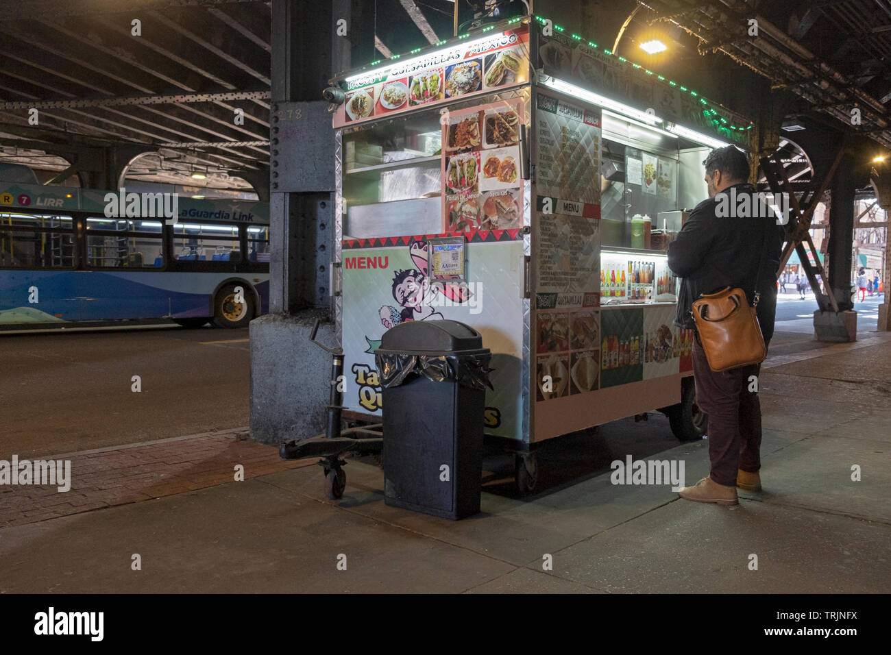 On his way home from work, a man buys fast food from a Mexican food cart under the el in Woodside, Queens, New York. Stock Photo