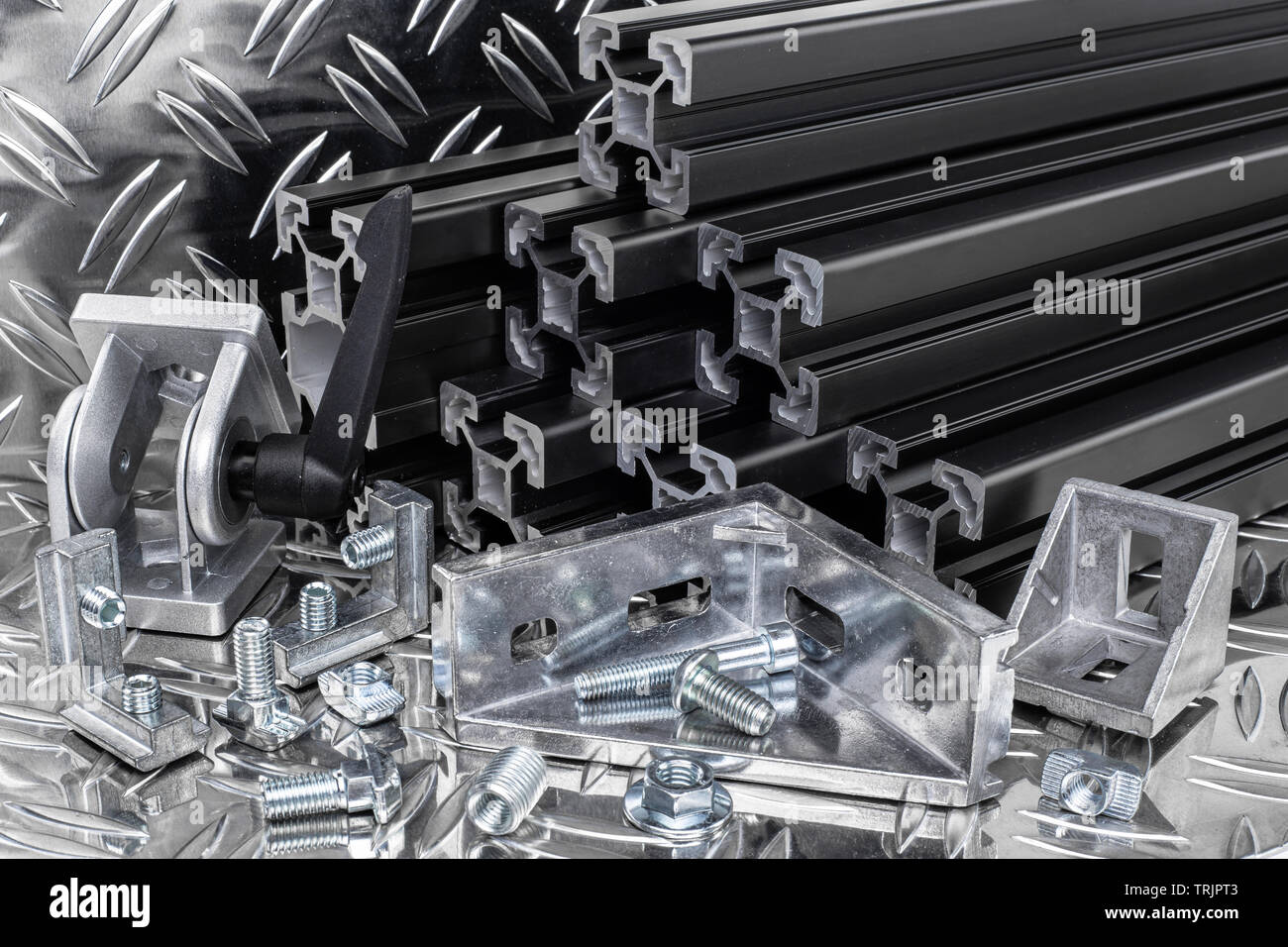 stack of black anodized aluminum extrusion bars, connector, joint, screw , slot nut and angle bracket on silver shiny diamond plate background. Constr Stock Photo