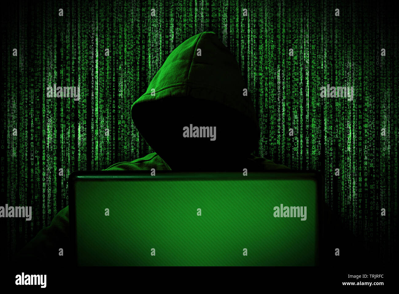 hacker with glowing mask behind notebook laptop in front of green source binary code background internet cyber hack attack computer concept Stock Photo