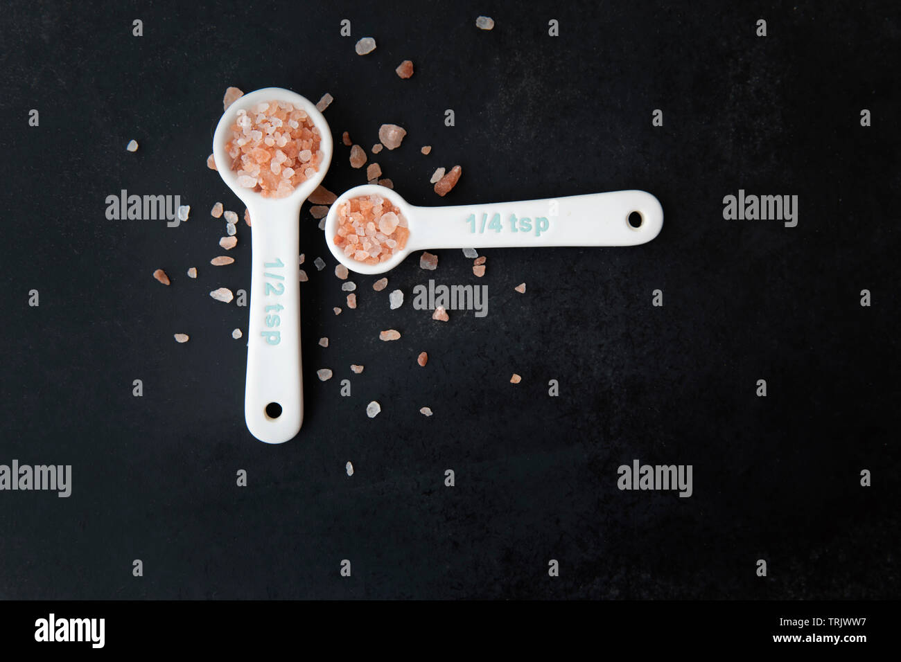Pink Himalayan salt in measuring spoons on black background. Stock Photo