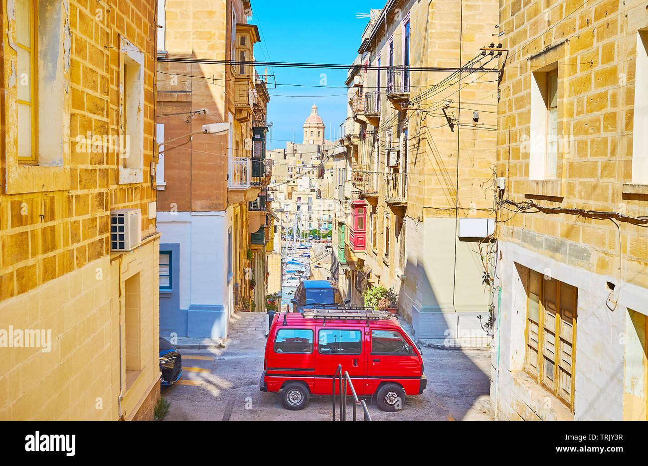 Walk down stairs in medieval Senglea with a view on old housing, parked retro mini bus and Vittoriosa marina on the background, Senglea, Malta Stock Photo